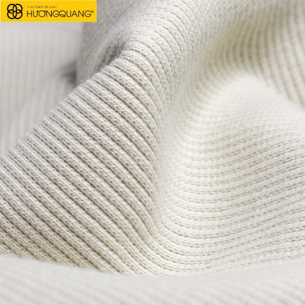 Vải dệt kim mềm rũ trên bàn may, ánh sáng chiếu làm nổi bật bề mặt vải